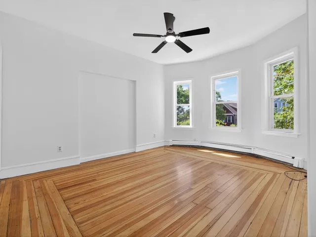 a view of empty room with wooden floor and fan