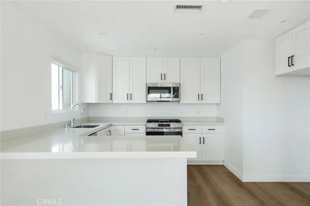 a kitchen with stainless steel appliances granite countertop a sink a stove a microwave a refrigerator a white cabinets and wooden floor