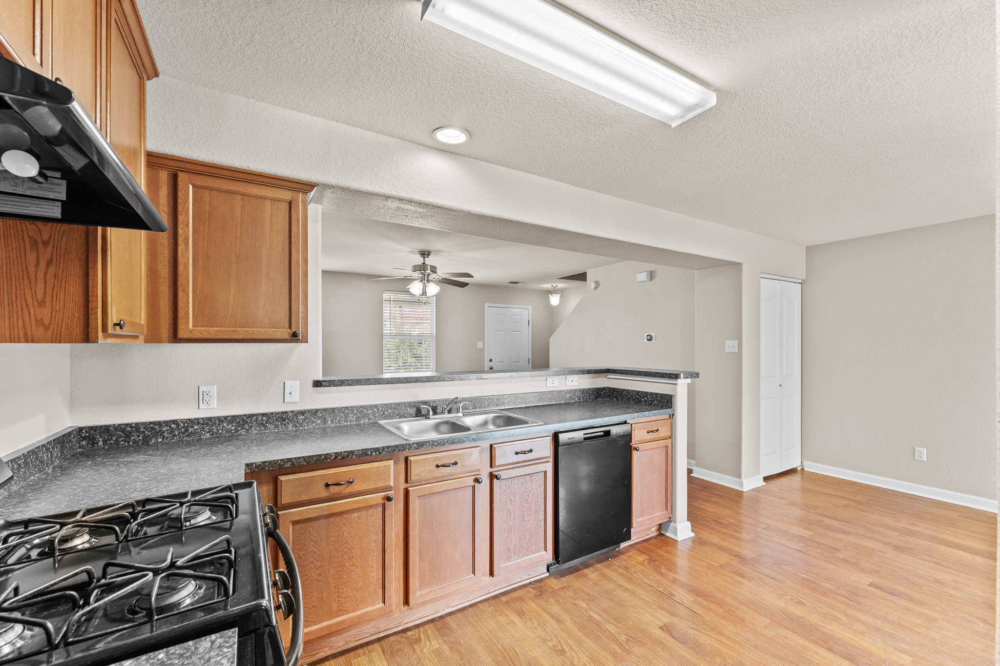 220 Trestle Tree San Marcos, TX 78666 - Photo 10 of 28 Kitchen with black appliances, a peninsula, ventilation hood, light wood-style flooring, and a textured ceiling
