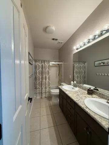 a spacious bathroom with a granite countertop sink a toilet a mirror and shower