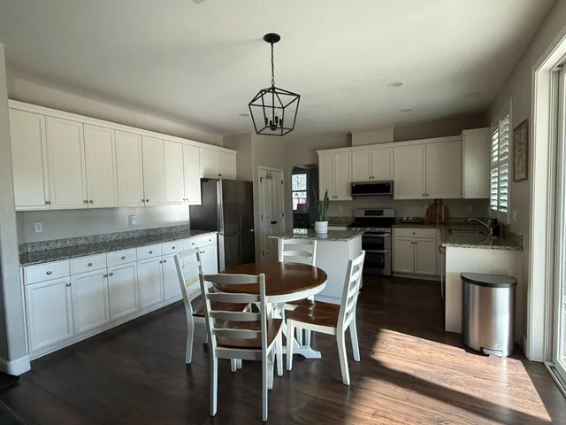 a kitchen with granite countertop a refrigerator a stove a sink dishwasher a dining table and chairs with wooden floor