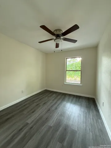 an empty room with wooden floor ceiling fan and windows