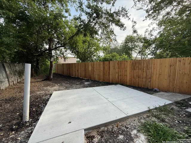 a view of backyard with white fence and trees