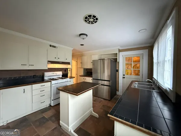 a kitchen with granite countertop a refrigerator a stove a sink and white cabinets with wooden floor