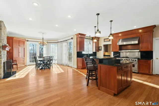 a kitchen with stainless steel appliances granite countertop a stove top oven a refrigerator a dining table and chairs with wooden floor