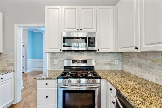a large kitchen with stainless steel appliances granite countertop a refrigerator a sink dishwasher a stove and white countertops with wooden floor