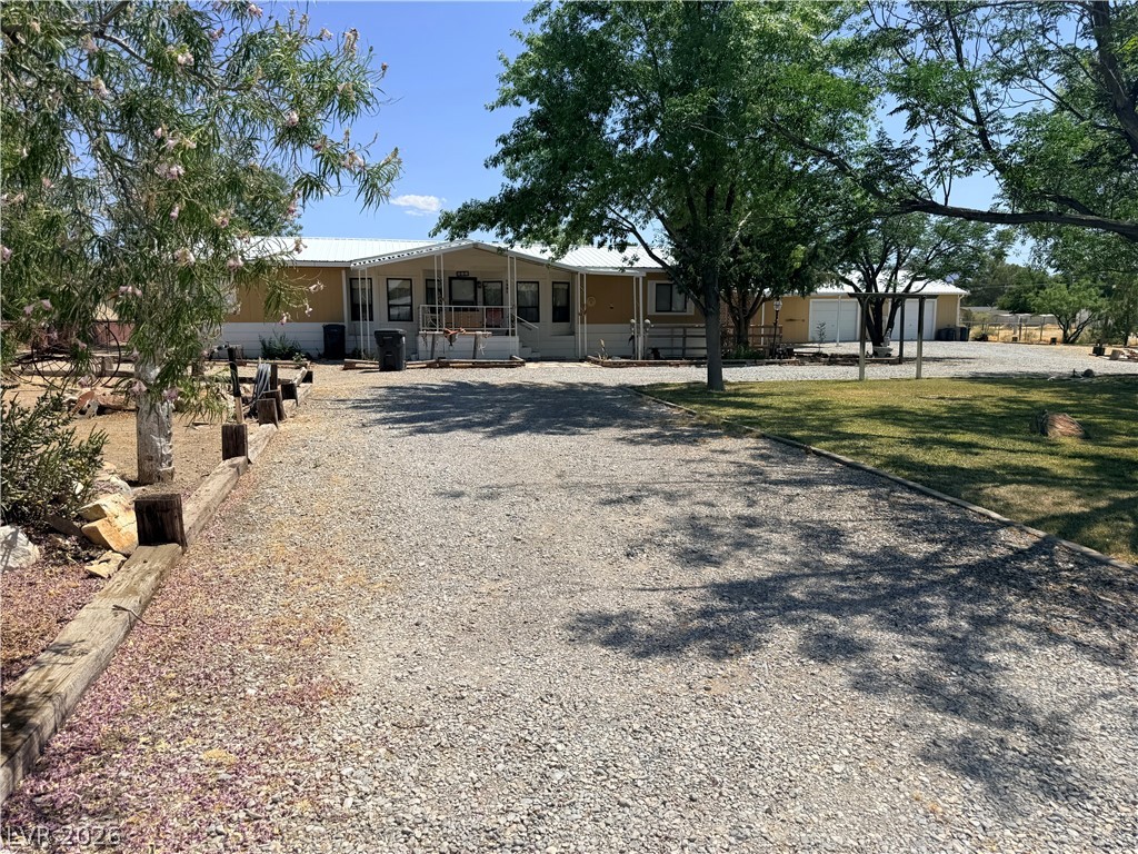 1391 West Dyer Road Pahrump, NV 89048 - Photo 3 of 50 A long gravel driveway leads to a secluded residence framed by mature trees and verdant landscaping.
