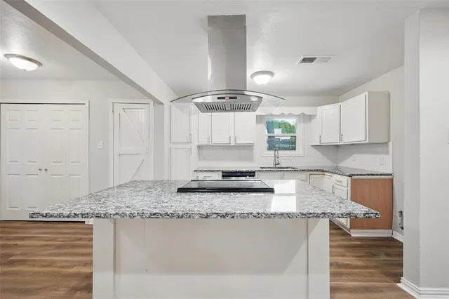 a kitchen with kitchen island granite countertop a sink cabinets and wooden floor