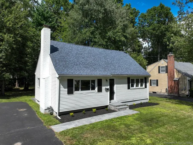 a view of a white house with a small yard and large trees