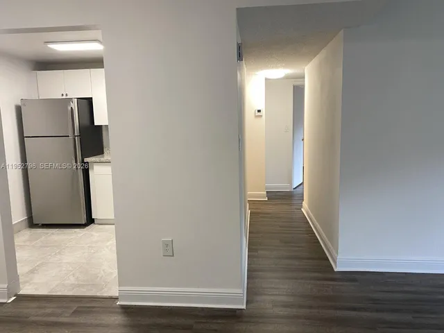a view of a refrigerator in kitchen and an empty room