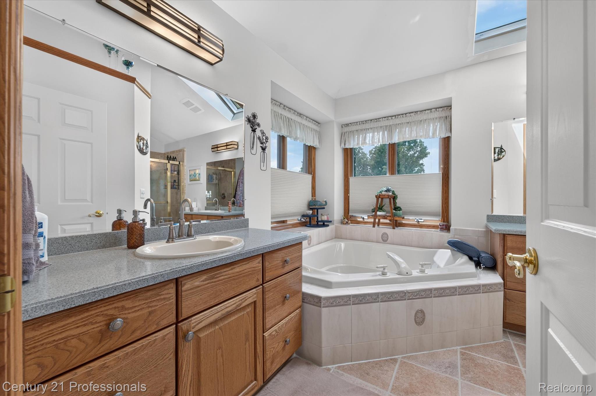 5675 36 Mile Road Romeo, MI 48065 - Photo 33 of 54 Spacious primary bathroom adjacent to primary bedroom featuring a large corner soaking tub with tiled surround, NOTE! separated vanities with a light-colored countertop and wood cabinetry, a skylight, and tiled flooring
