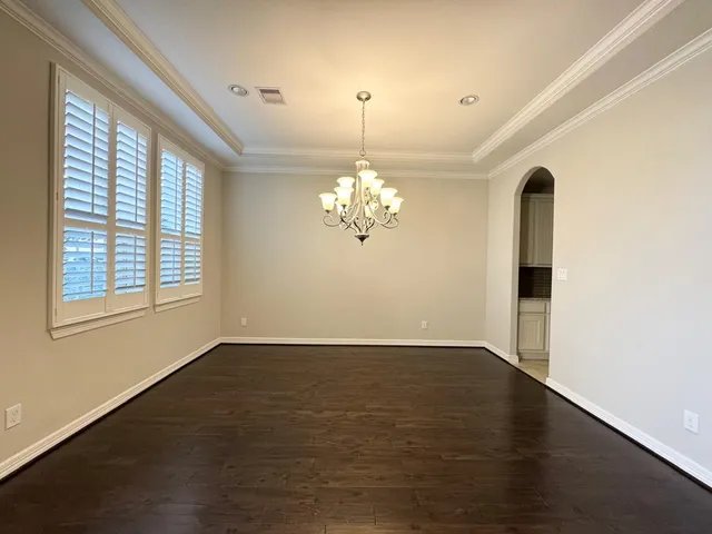an empty room with wooden floor chandelier and windows