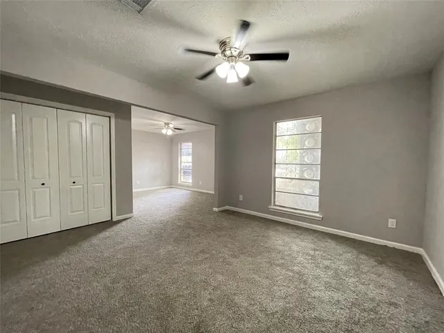 an empty room with chandelier fan and windows
