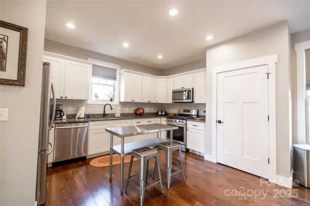 a kitchen with stainless steel appliances granite countertop a refrigerator a stove top oven a sink dishwasher and white cabinets with wooden floor