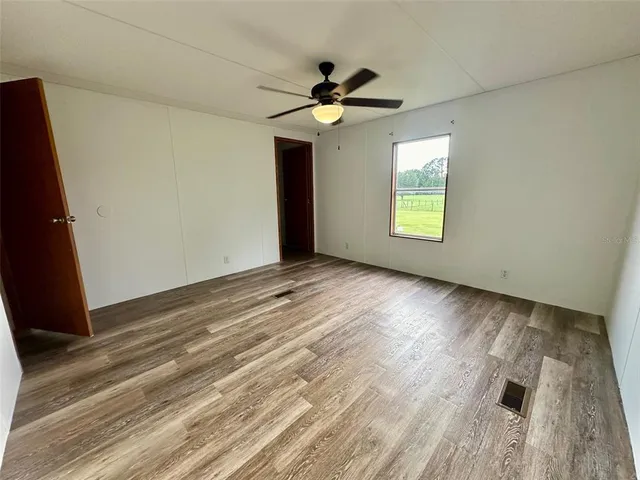 an empty room with wooden floor chandelier fan and windows