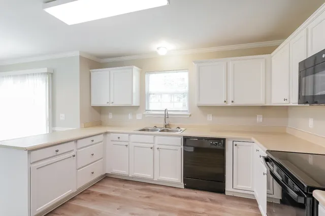 a kitchen with white cabinets appliances a sink and a window