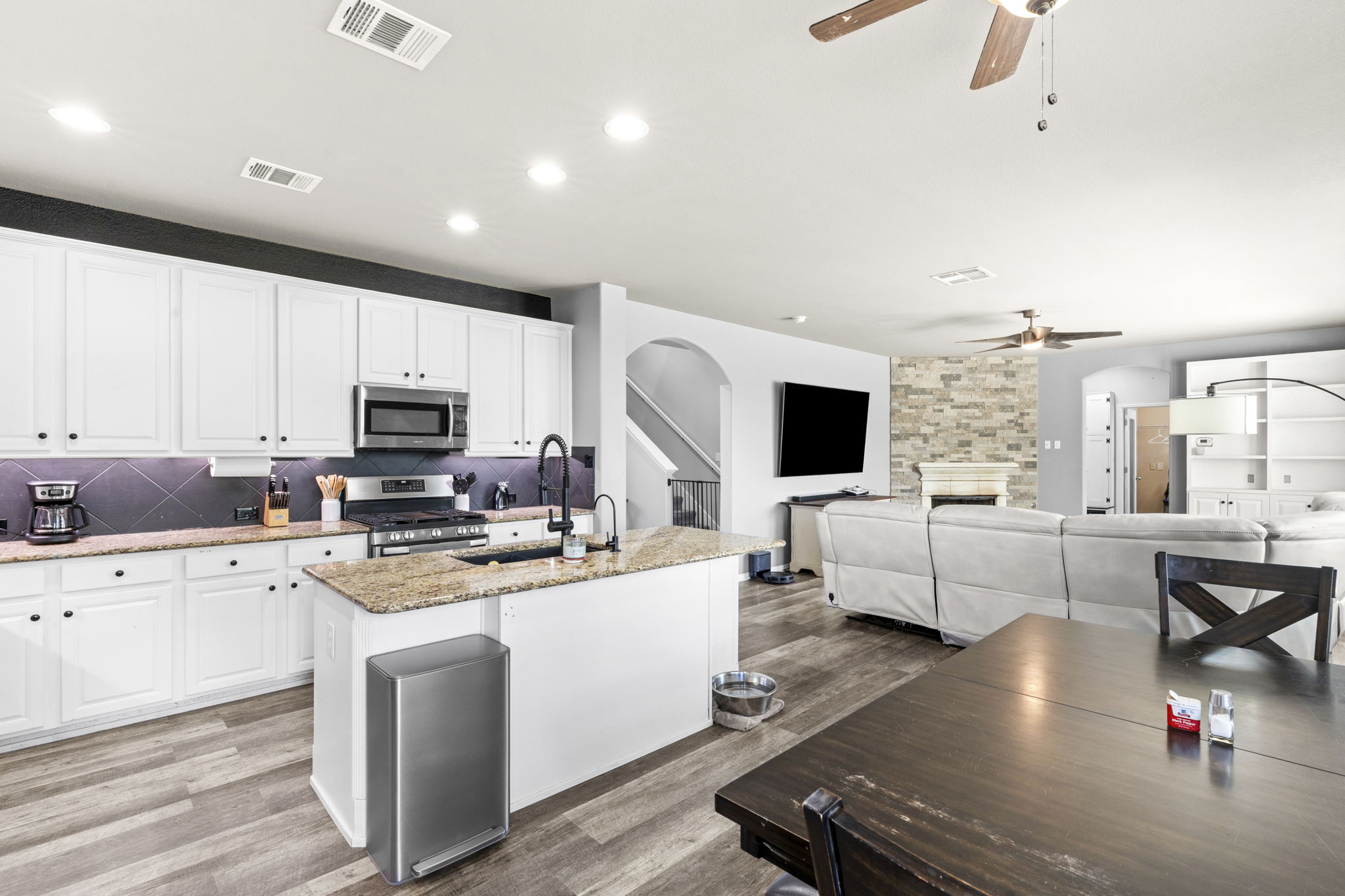 227 Sandstone Trail Buda, TX 78610 - Photo 7 of 33 Open-concept living area featuring a kitchen island with granite countertops, white cabinetry with dark hardware, stainless steel appliances, and wood-finish flooring