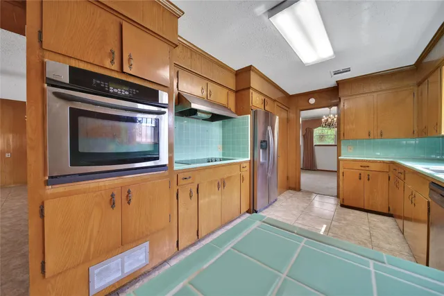 a kitchen with stainless steel appliances kitchen island granite countertop a refrigerator a stove and wooden cabinets