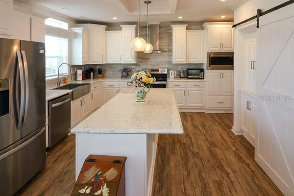 a kitchen with stainless steel appliances a refrigerator a stove top oven a sink dishwasher and white cabinets with wooden floor