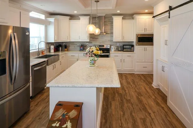 a kitchen with stainless steel appliances a refrigerator a stove top oven a sink dishwasher and white cabinets with wooden floor