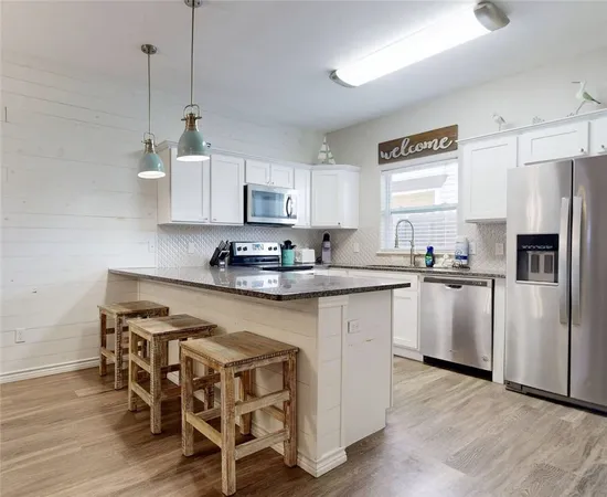 a kitchen with stainless steel appliances granite countertop a refrigerator a stove a sink dishwasher and white cabinets with wooden floor