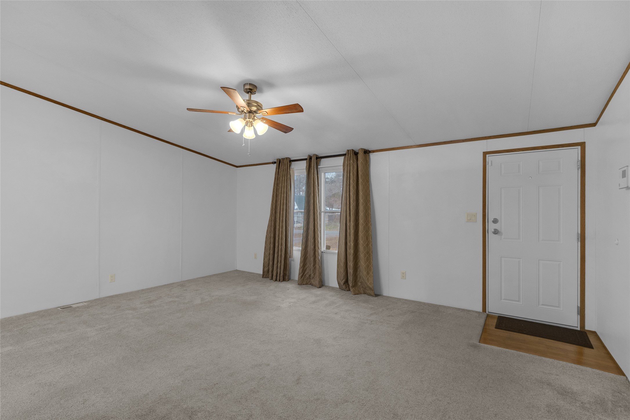 22094 Spear Road Porter, TX 77365 - Photo 18 of 45 A cozy living room with neutral carpet, a ceiling fan, and a large window with curtains. The space features a simple entry door and clean white walls, offering a bright and inviting atmosphere.