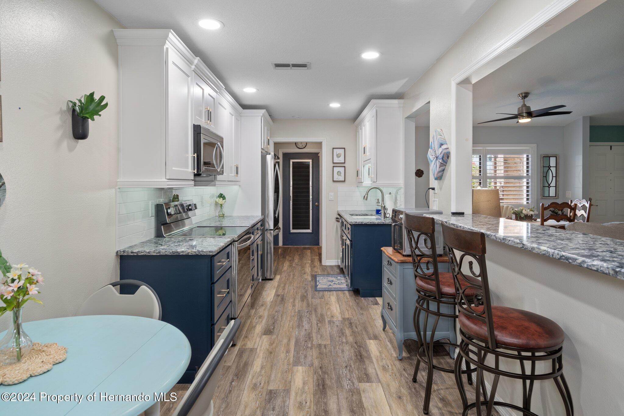 7427 Heather Walk Drive Spring Hill, FL 34613 - Photo 16 of 36 a kitchen with stainless steel appliances granite countertop a kitchen island hardwood floor sink stove dining table and chairs