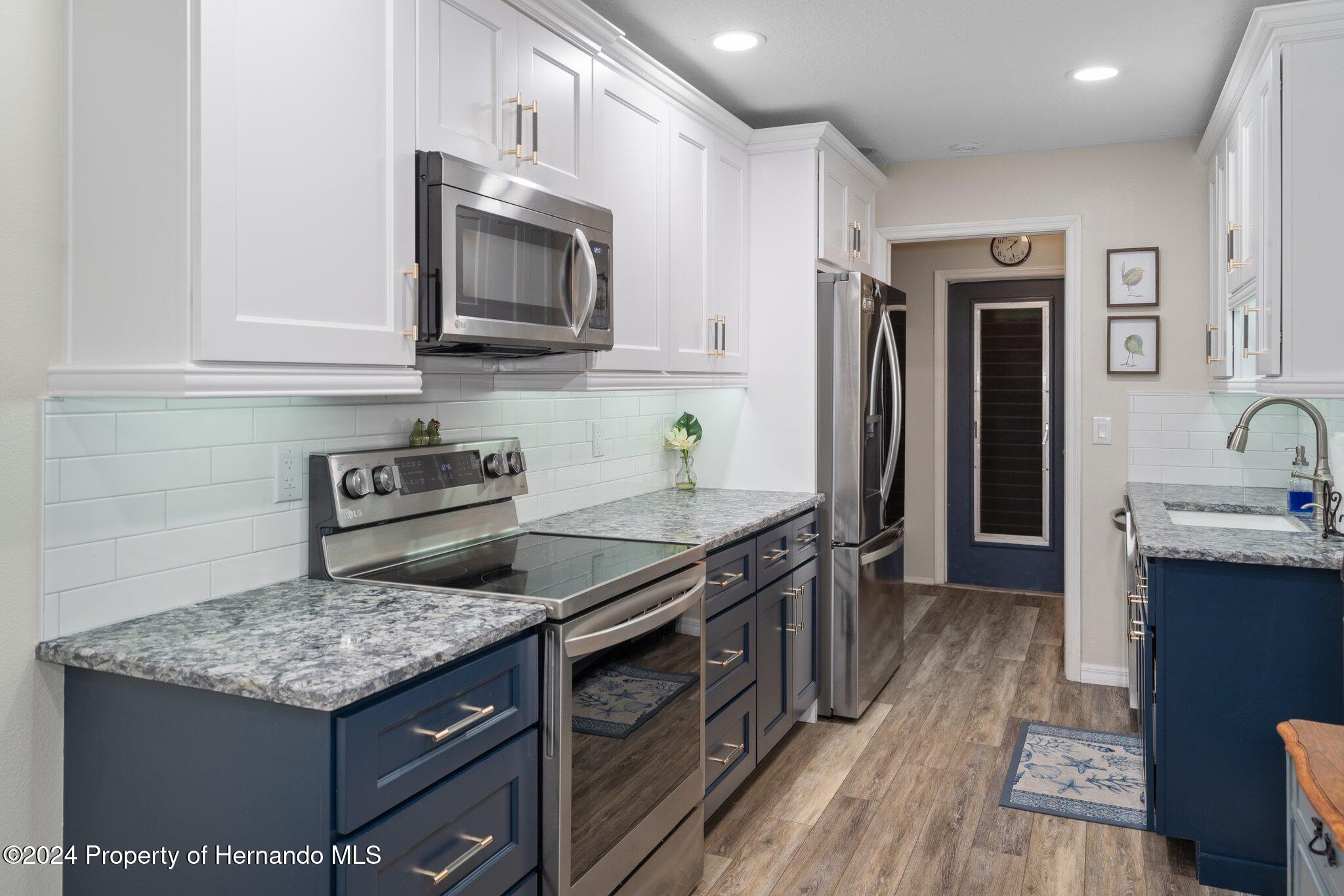 7427 Heather Walk Drive Spring Hill, FL 34613 - Photo 18 of 36 a kitchen with stainless steel appliances granite countertop a stove top oven a sink dishwasher a refrigerator and a oven with wooden floor