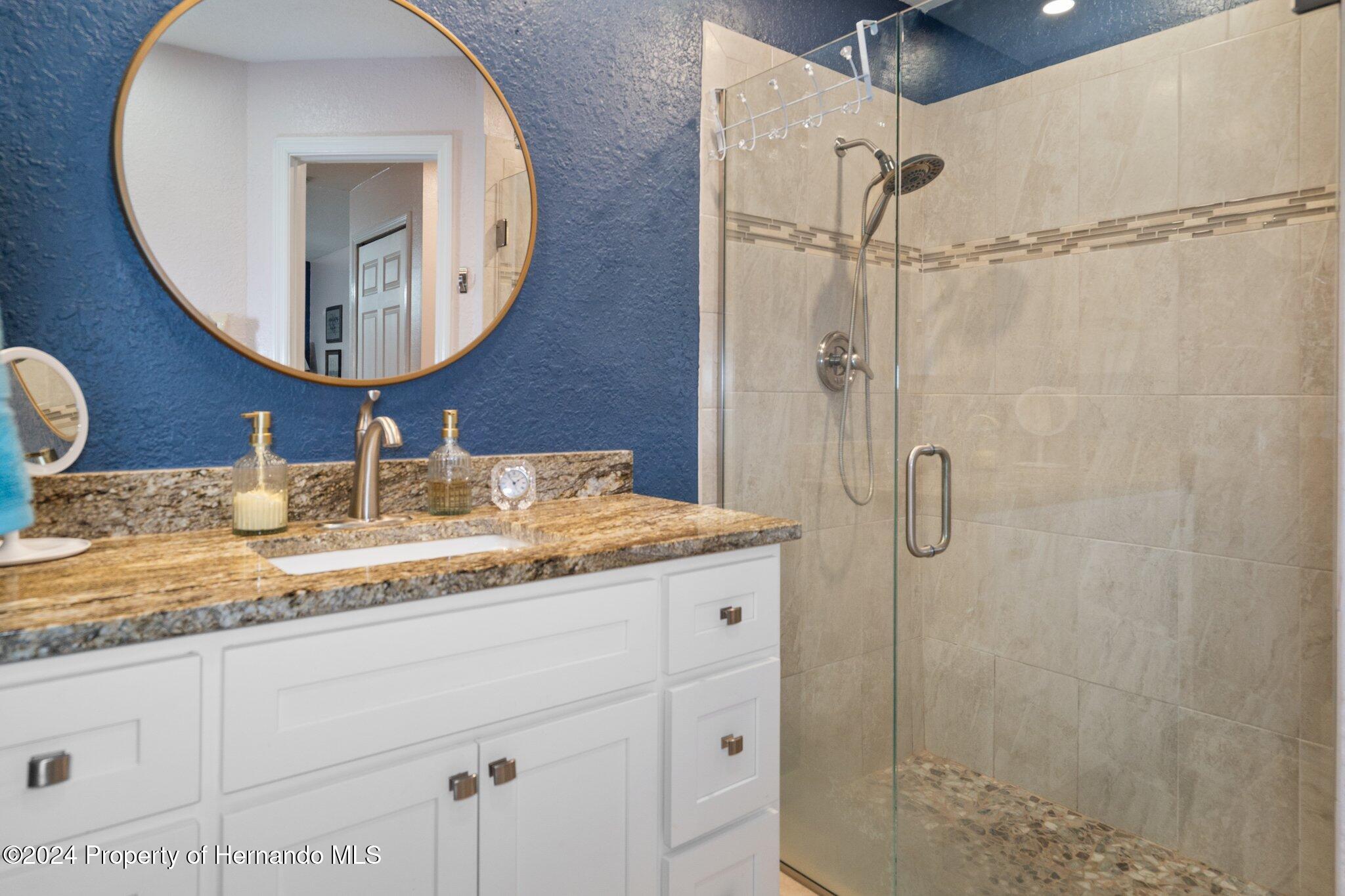 7427 Heather Walk Drive Spring Hill, FL 34613 - Photo 30 of 36 a bathroom with a granite countertop sink a mirror and shower