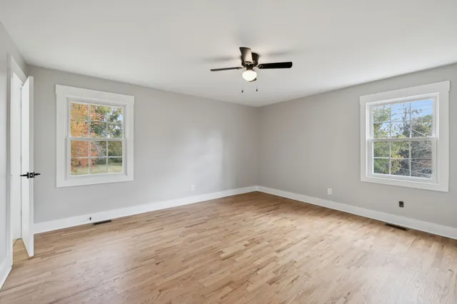 an empty room with wooden floor ceiling fan and windows