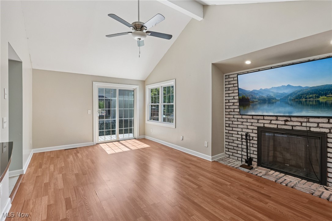 159 Eastland Road Berea, OH 44017 - Photo 7 of 38 Unfurnished living room featuring high vaulted ceiling, wood finished floors, beam ceiling, a brick fireplace, and a ceiling fan