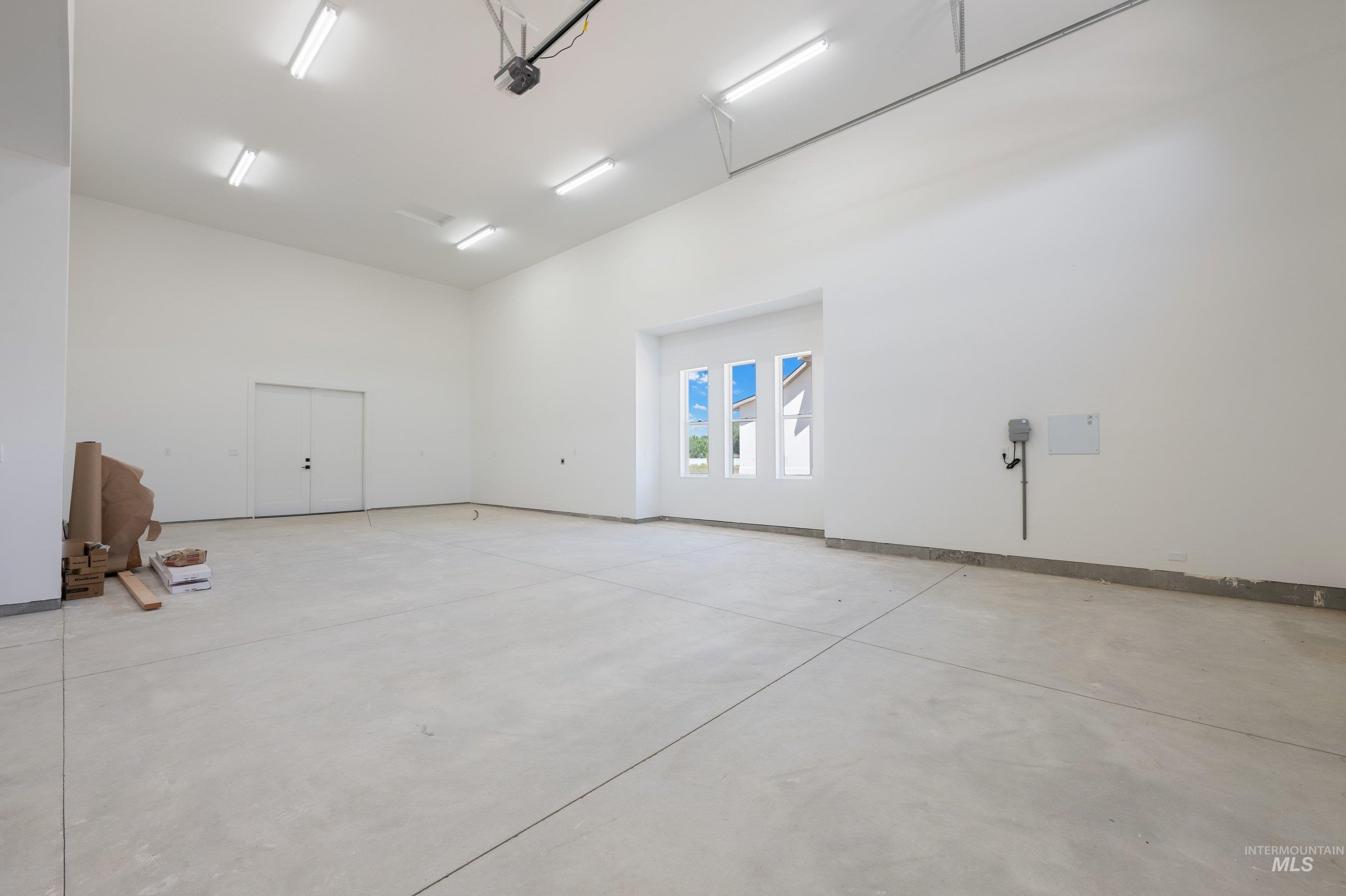 24821 Ardmore Court Caldwell, ID 83607 - Photo 36 of 43 Spacious garage featuring a concrete floor, high ceilings, multiple fluorescent lighting fixtures, and three transom windows