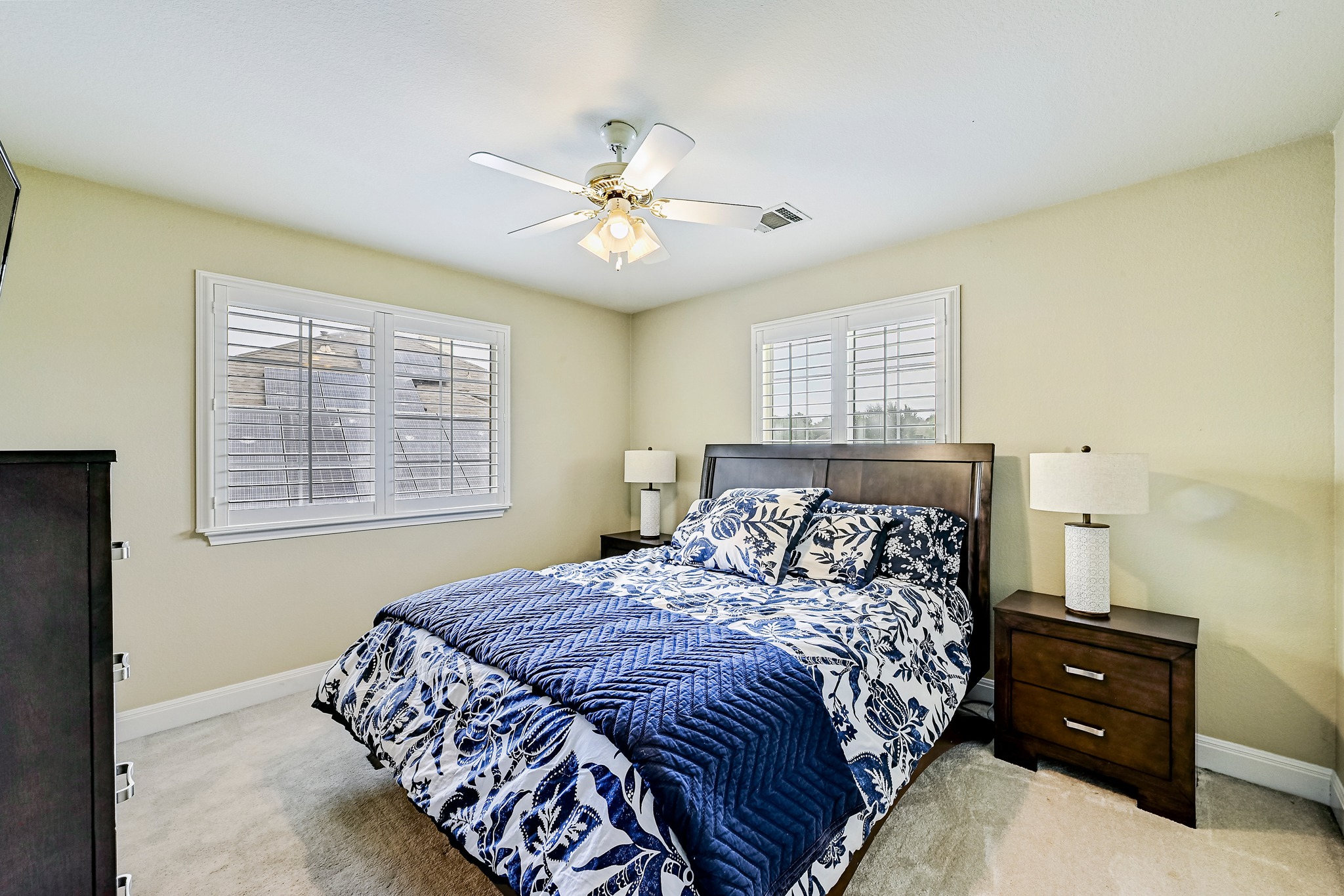 2408 Amen Corner Road Pflugerville, TX 78660 - Photo 29 of 40 Carpeted bedroom featuring two windows with white plantation shutters, a dark wood headboard, and a ceiling fan with integrated lighting