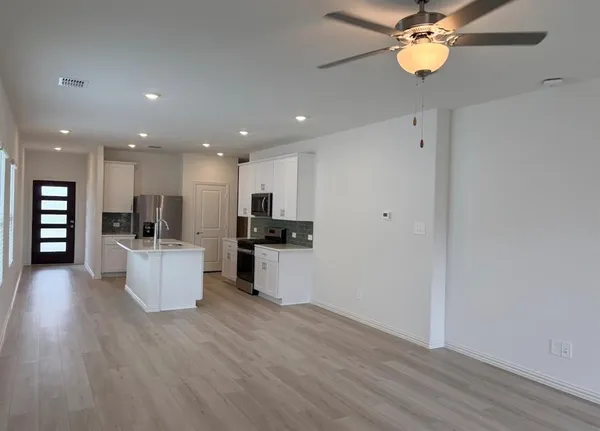 a view of kitchen with kitchen island stainless steel appliances refrigerator stove and wooden floor