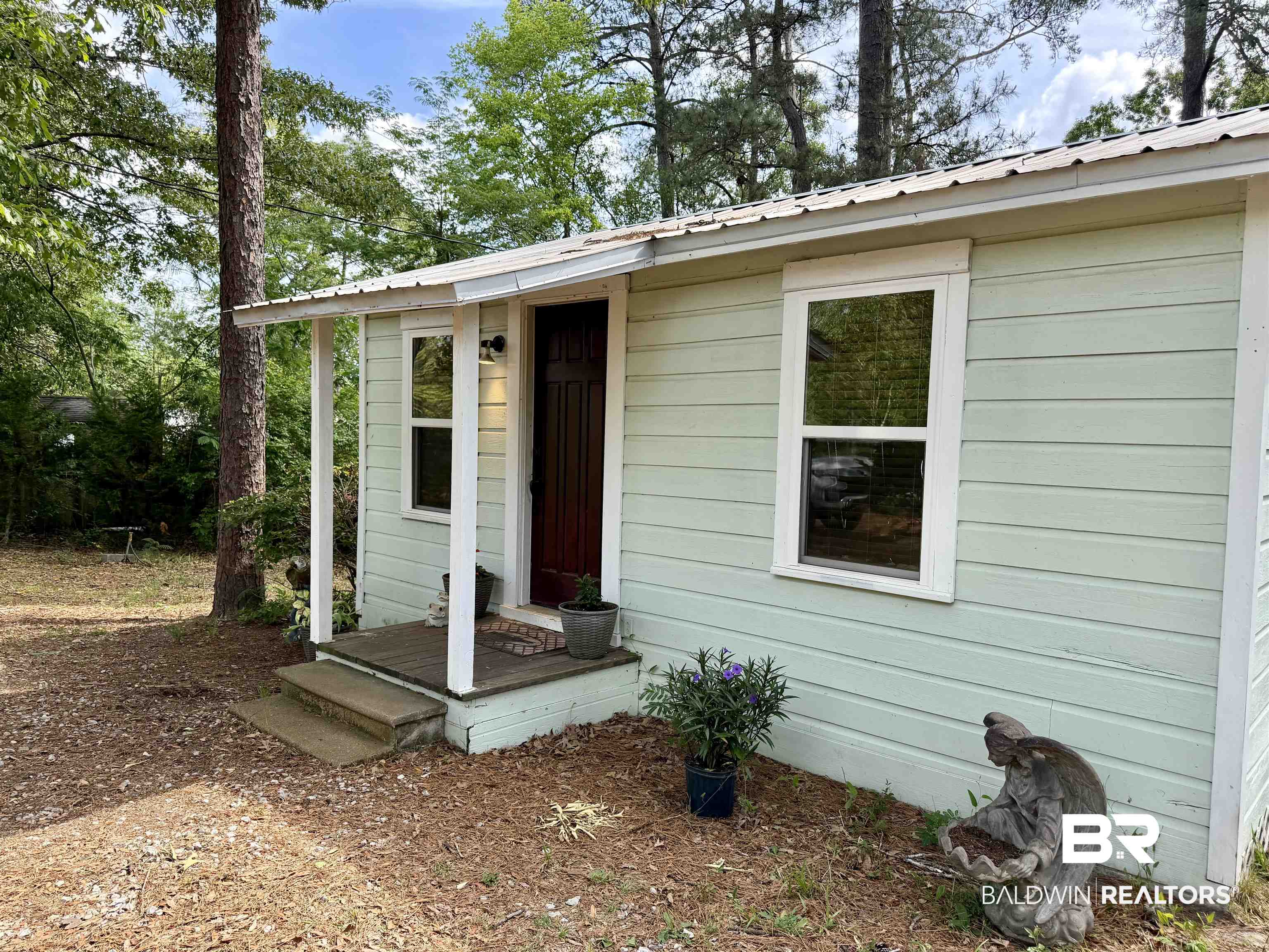 762 Buddy Lake Road Brewton, AL 36426 - Photo 5 of 20 Mint green siding exterior featuring a covered porch entry, white trim windows, and a dark wood-finish entry door