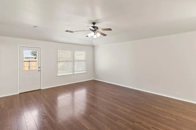 a view of an empty room with wooden floor and a window