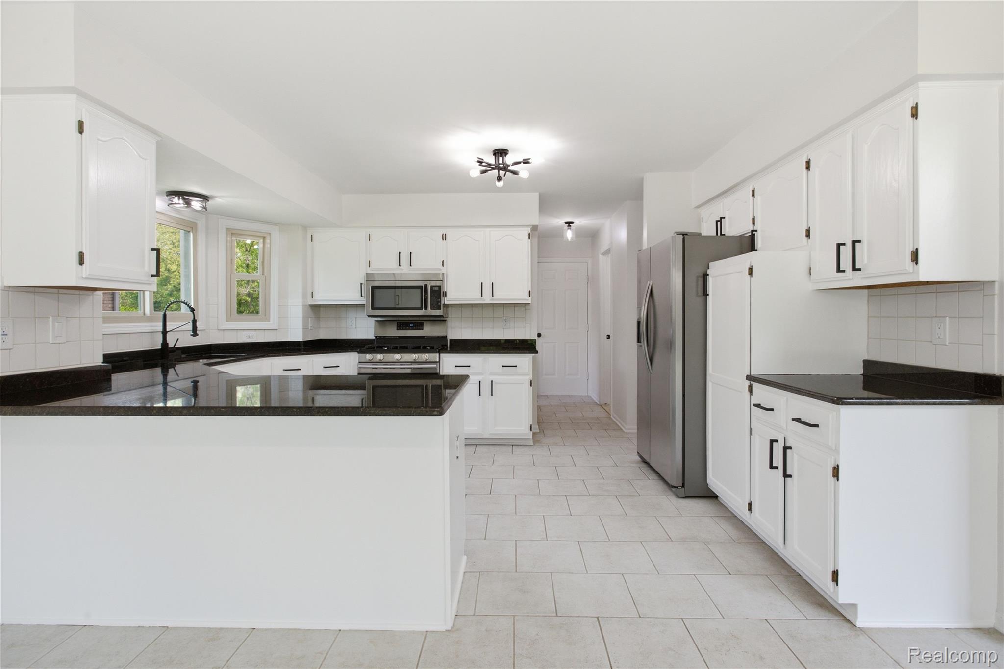 52658 Stag Ridge Drive Macomb, MI 48042 - Photo 11 of 28 Spacious kitchen featuring white cabinetry, dark countertops, stainless steel appliances, a tile backsplash, and light tile flooring