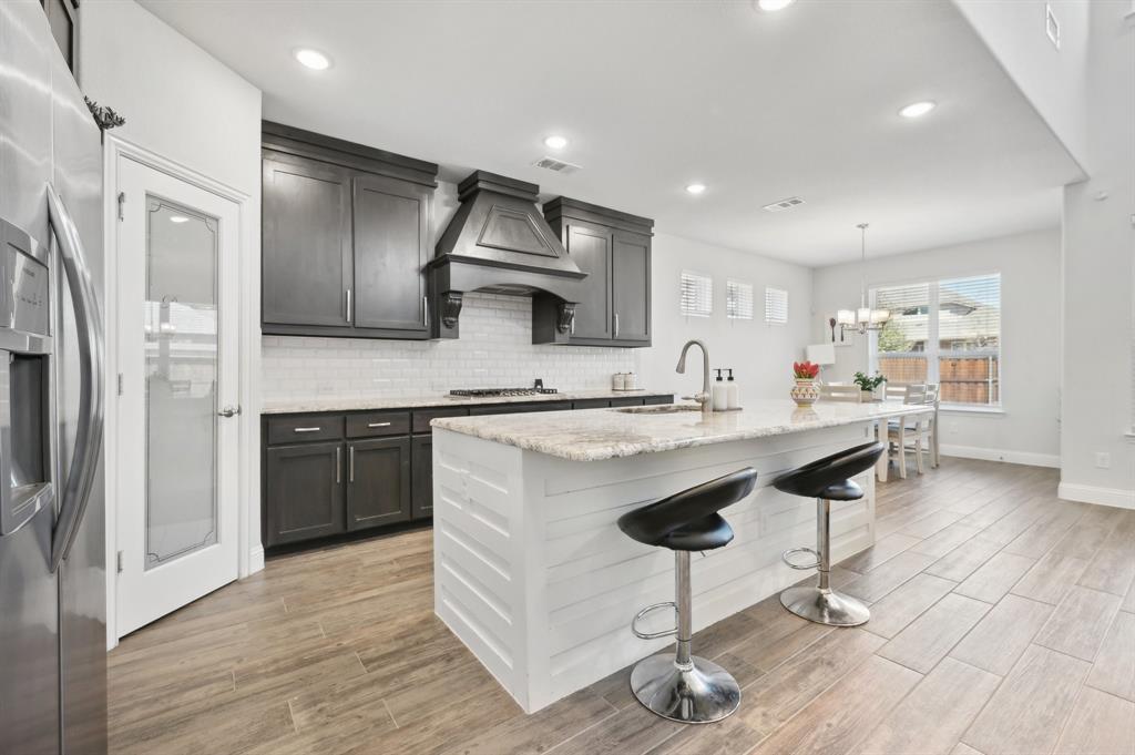 2172 Poppyvine Road Frisco, TX 75033 - Photo 12 of 40 Kitchen featuring stainless steel appliances, a kitchen breakfast bar, light stone countertops, and wood finish floors