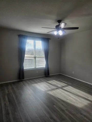 an empty room with wooden floor chandelier fan and windows