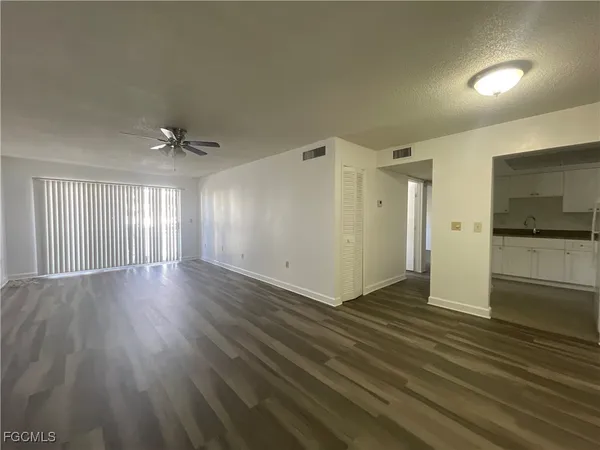 an empty room with wooden floor and a kitchen