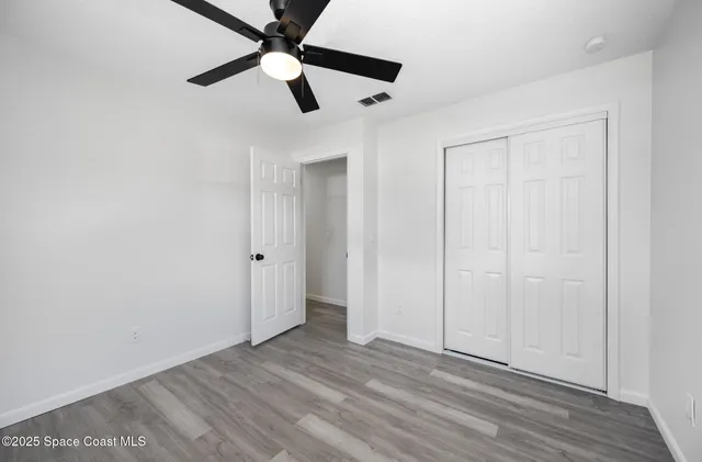 an empty room with wooden floor ceiling fan and windows