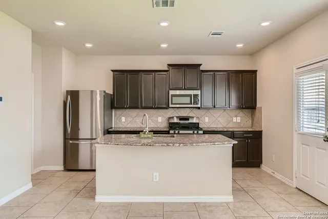 a kitchen with kitchen island granite countertop a refrigerator oven a sink and dishwasher