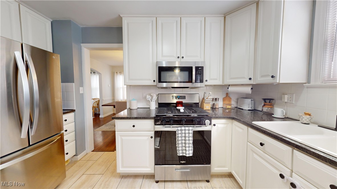 4042 Bushnell Road University Heights, OH 44118 - Photo 10 of 37 Kitchen featuring white cabinets, tasteful backsplash, appliances with stainless steel finishes, dark stone countertops, and light wood-type flooring