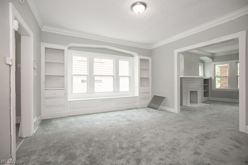 1000 Eddy Road Cleveland, OH 44108 - Photo 8 of 38 Unfurnished living room with crown molding, carpet floors, a brick fireplace, and a textured ceiling