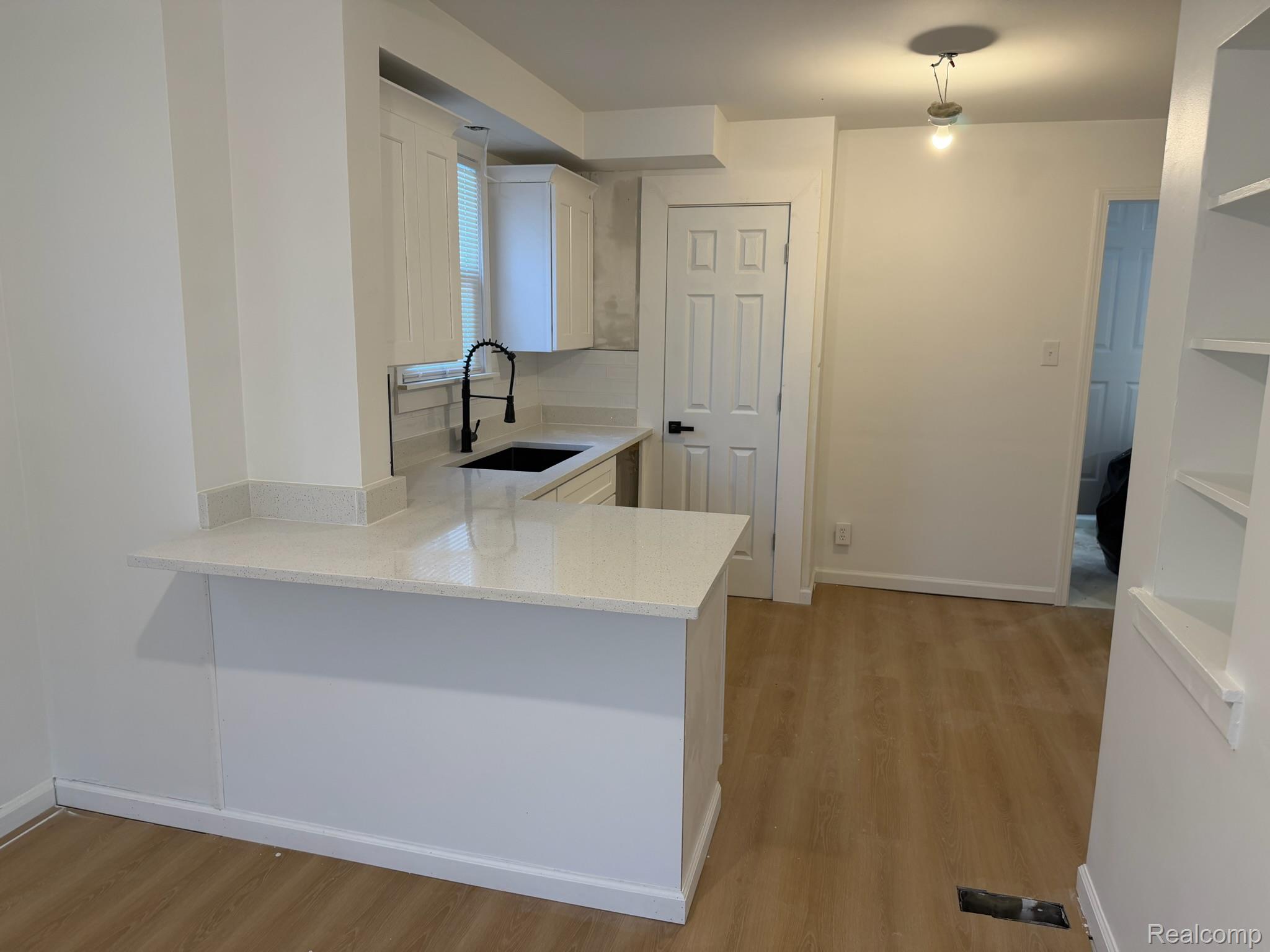 9869 Yorkshire Road Detroit, MI 48224 - Photo 4 of 14 White shaker cabinetry, light-toned countertops, black single-handle faucet, wood-finish flooring, and built-in shelving