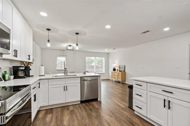 a kitchen with stainless steel appliances a stove top oven a sink dishwasher and white cabinets with wooden floor