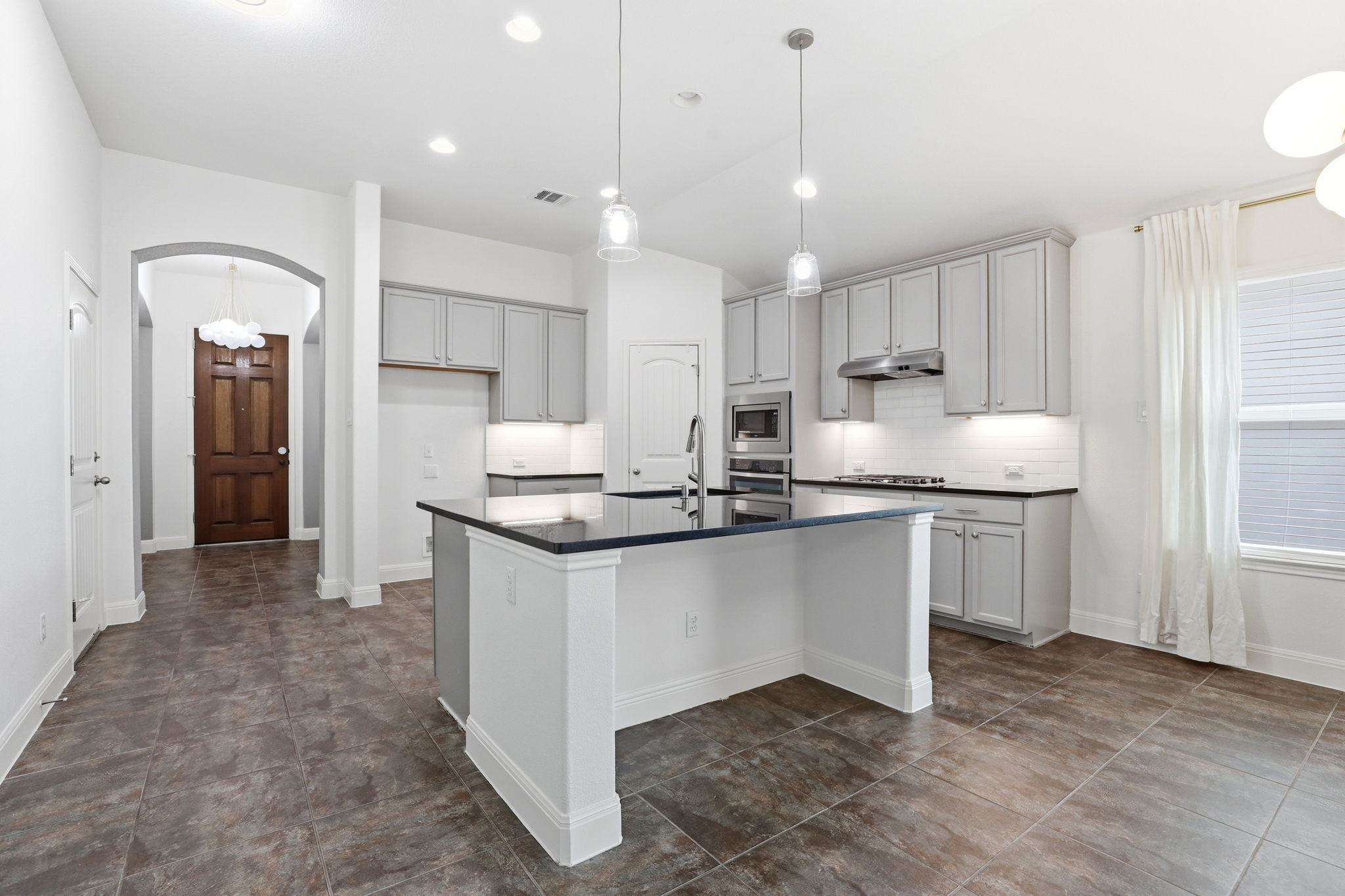 152 Stone View Trail Austin, TX 78737 - Photo 10 of 33 Kitchen featuring arched walkways, lofted ceiling, an island with sink, gray cabinetry, and stainless steel appliances