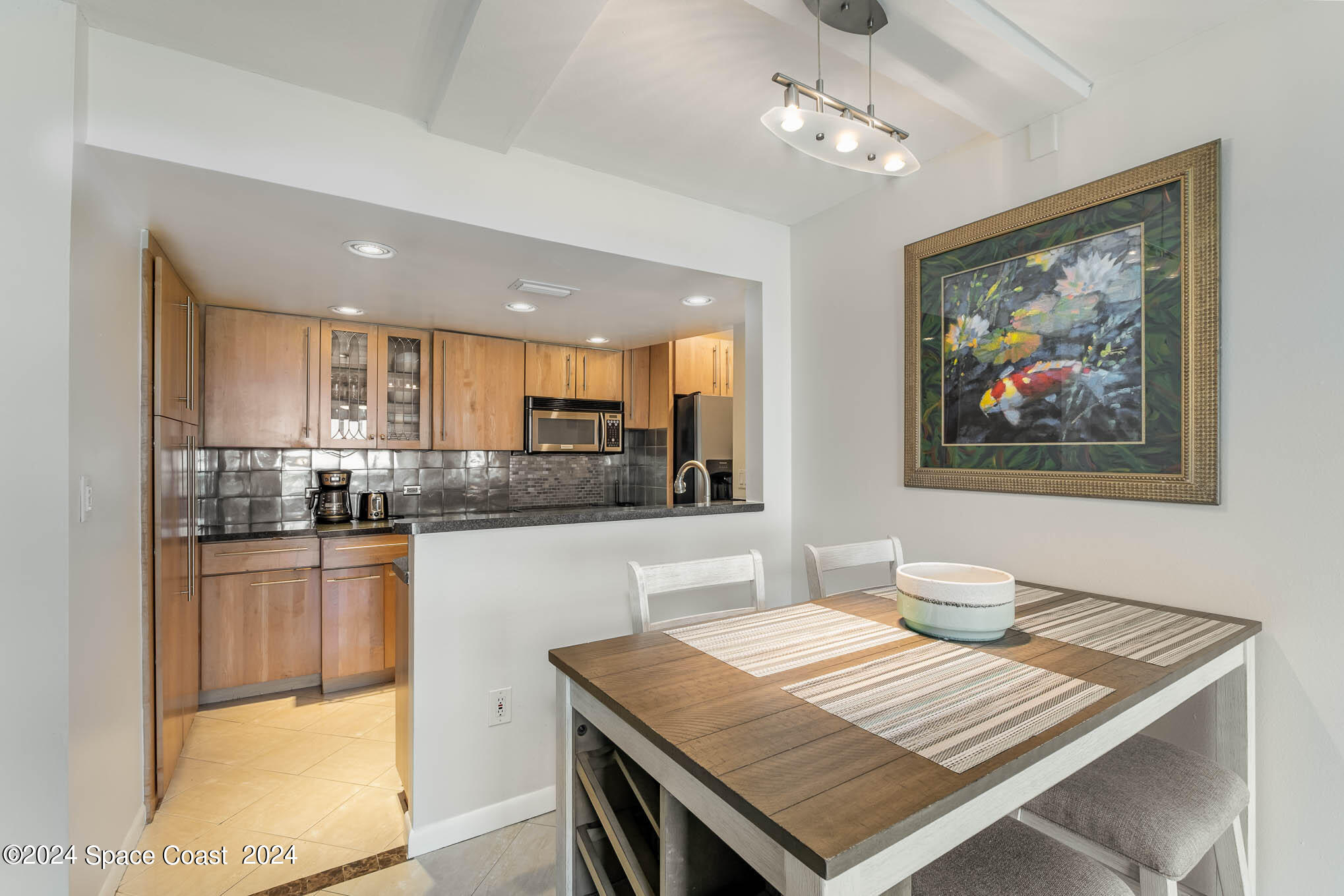 4800 Ocean Beach Boulevard, Unit 311 Cocoa Beach, FL 32931 - Photo 7 of 22 a open kitchen with stainless steel appliances granite countertop a stove top oven a sink a dining table and chairs with wooden floor