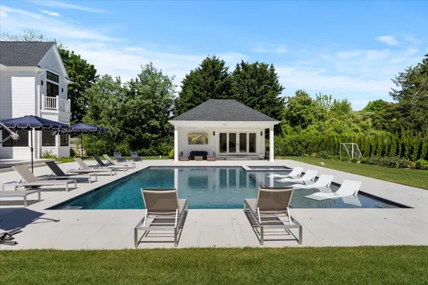 a white house with a large pool lawn chairs and a yard