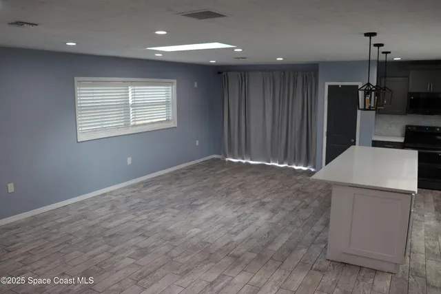 an empty room with kitchen view and wooden floor